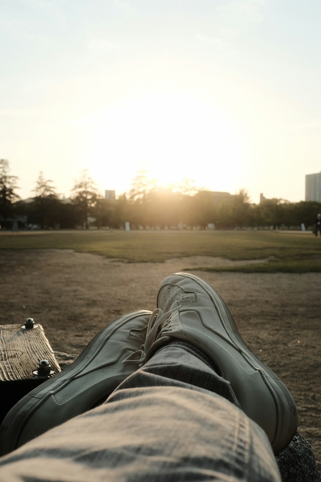 person in blue denim jeans and white sneakers lying on brown wooden bench during daytime