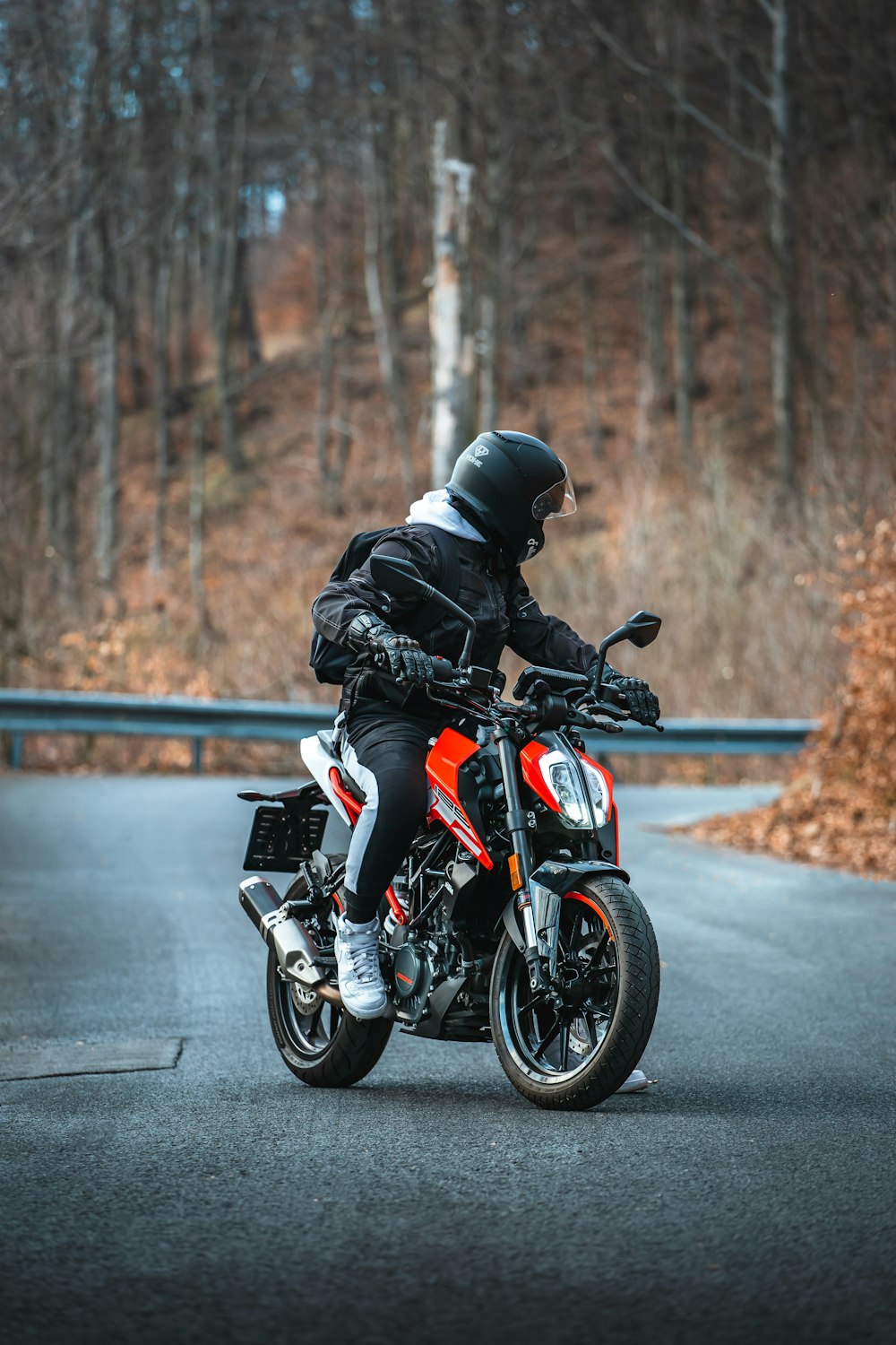 낮 동안 도로에서 주황색과 검은색 오토바이를 타는 검은색 재킷을 입은 남자