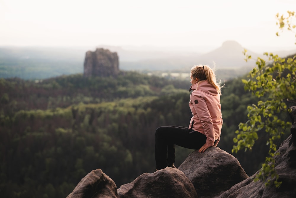 femme en veste marron assise sur le rocher pendant la journée