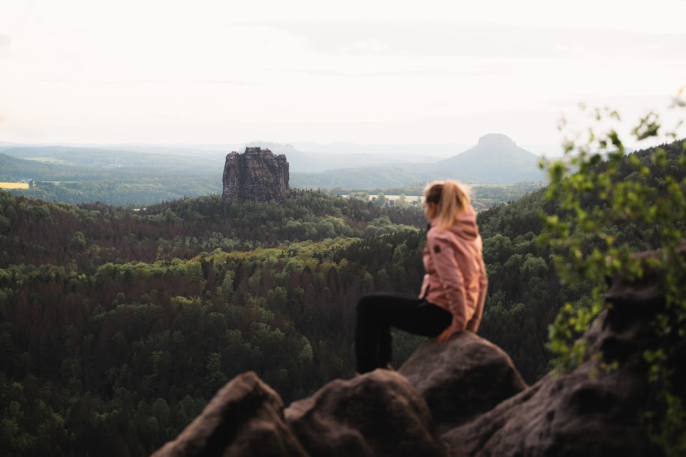 woman in brown jacket and black pants sitting on rock formation during daytime