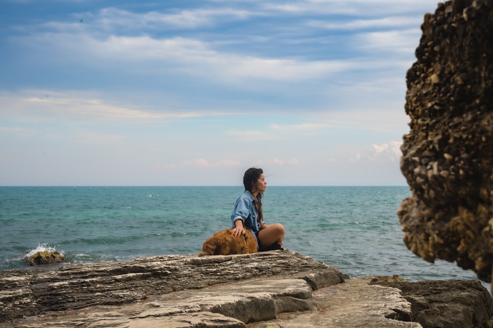 昼間、海近くの茶色の岩の上に座る青いシャツの男