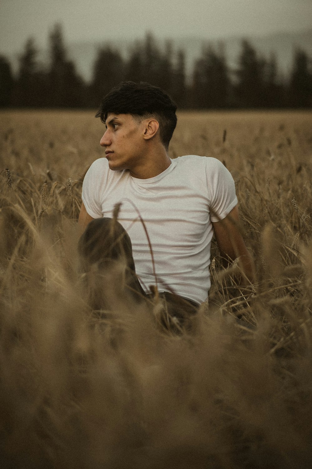 Uomo in maglietta bianca a girocollo che si siede sul campo di erba marrone durante il giorno