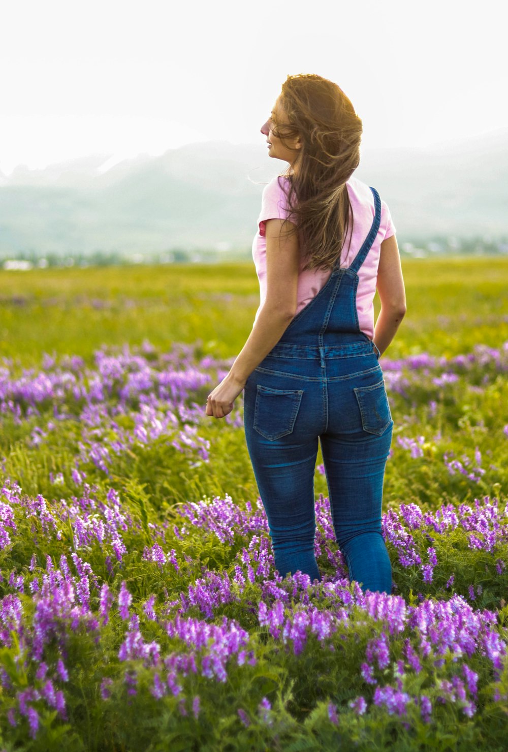 Mujer con camiseta blanca sin mangas y jeans de mezclilla azul de pie en el campo de flores púrpuras durante el día