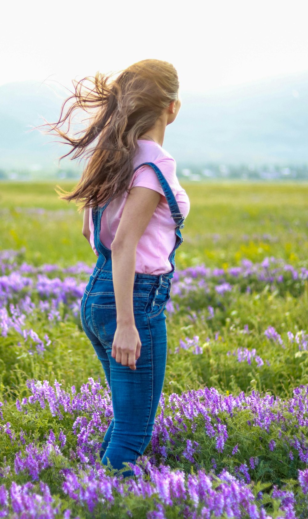 mulher na camisa branca e jeans jeans azuis de pé no campo de flores roxas durante o dia