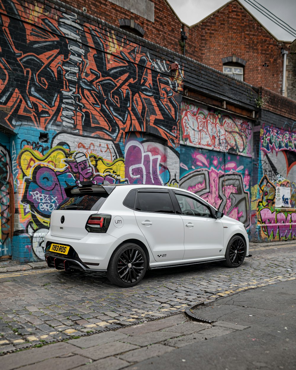 white sedan parked beside wall with graffiti