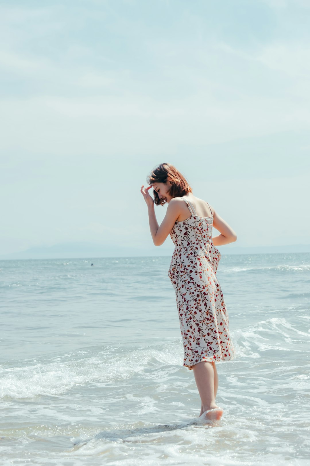 woman in white and black floral dress standing on seashore during daytime