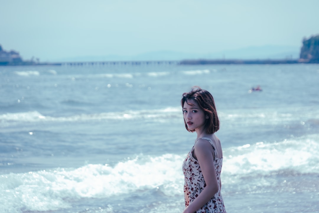 woman in white and black floral tank top standing near sea during daytime