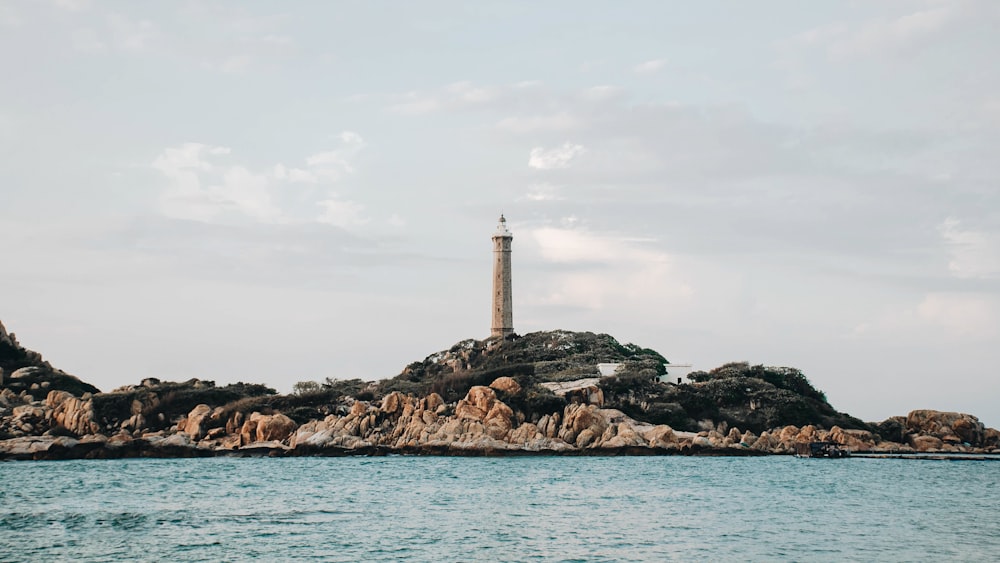 white and brown lighthouse on brown rock formation near body of water during daytime