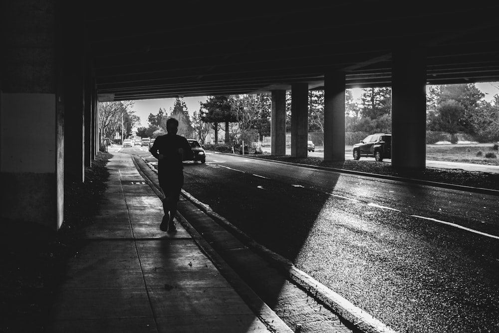 grayscale photo of man walking on sidewalk