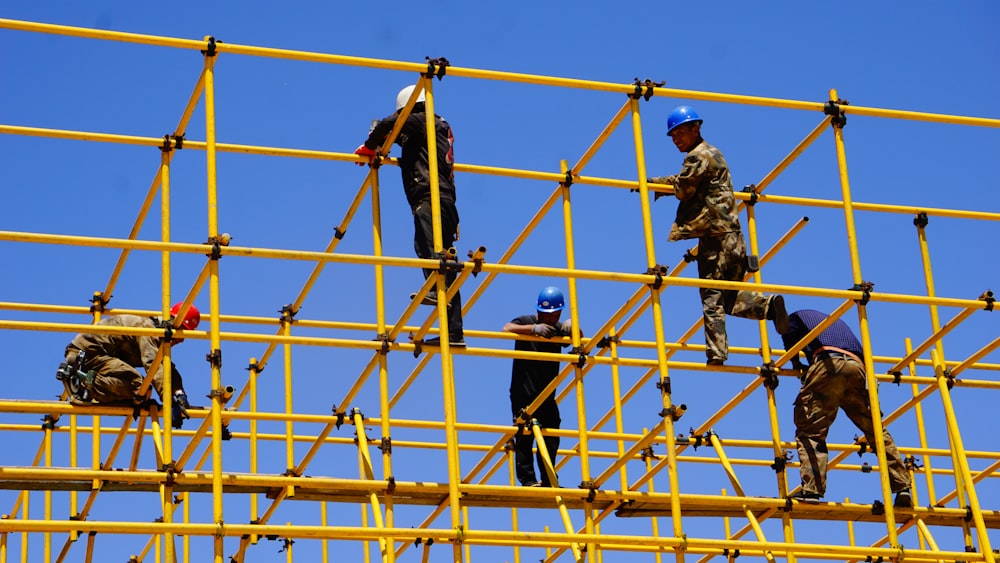 3 men standing on yellow metal fence during daytime