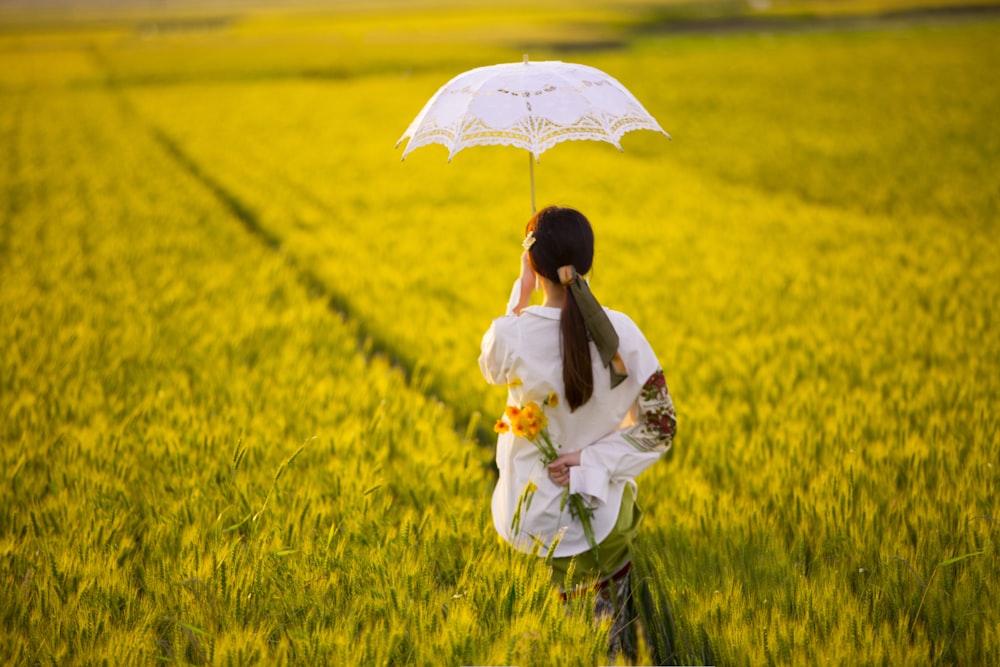 woman in white dress holding umbrella standing on green grass field during daytime