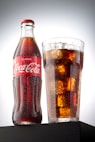 coca cola bottle beside drinking glass