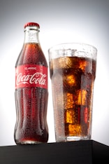 coca cola bottle beside drinking glass