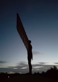 A majestic guardian angel with outstretched wings overlooking a misty British countryside at dawn.