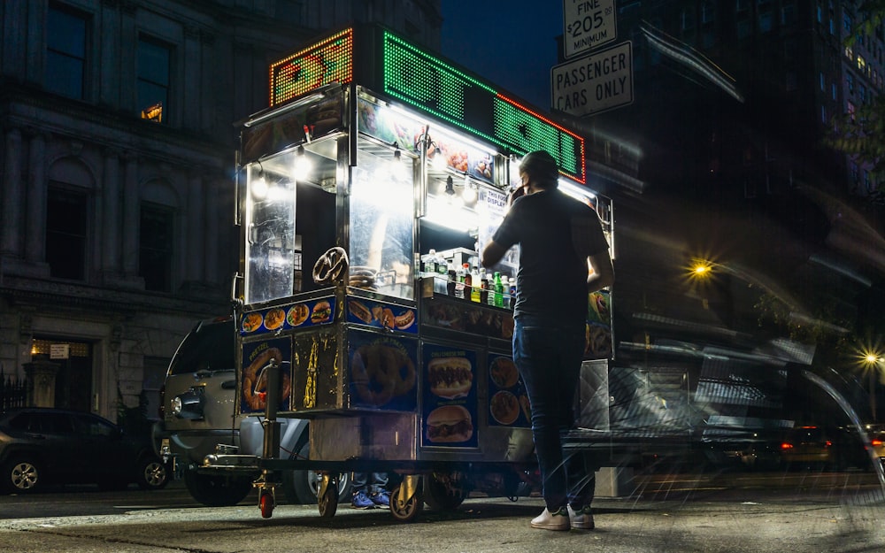 man in black jacket standing beside blue and yellow food cart