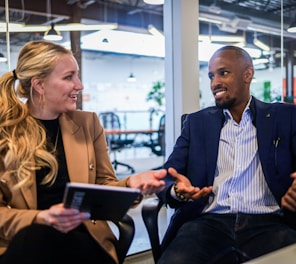 man in black suit jacket sitting beside woman in brown blazer