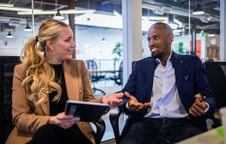 man in black suit jacket sitting beside woman in brown blazer