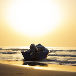 blue boat on sea shore during sunset