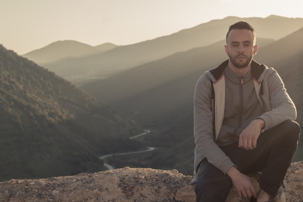 man in gray zip up jacket sitting on brown rock during daytime