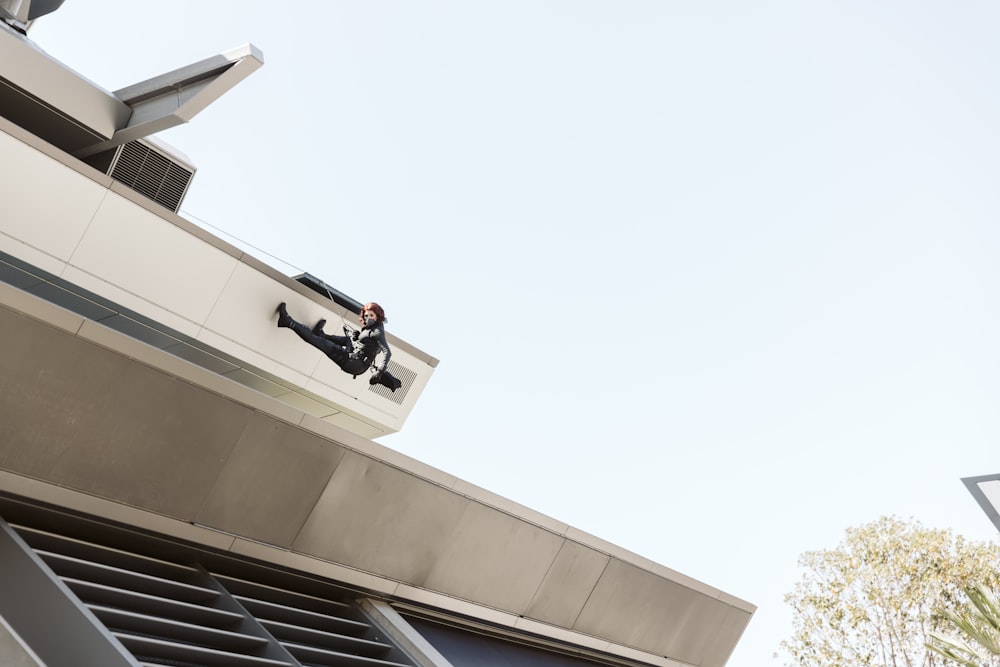 man in black jacket and black pants sitting on white concrete building during daytime