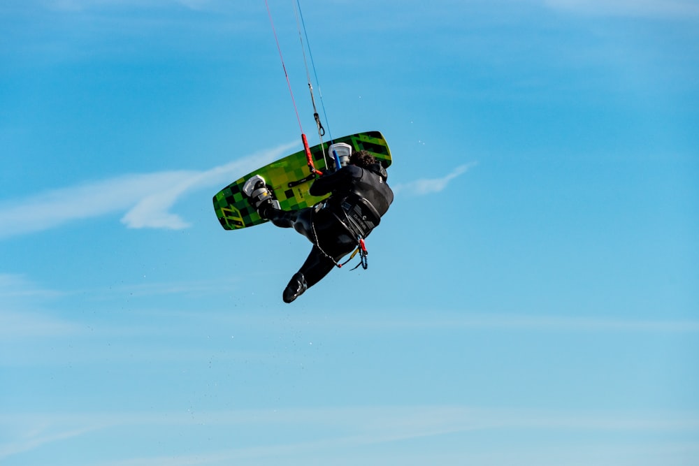 man in green and black jacket and black pants riding green and black snowboard during daytime