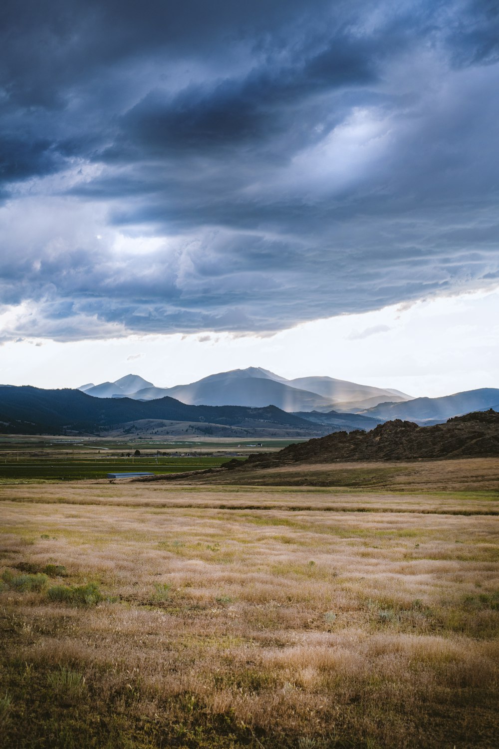 brown grass field near mountains under white clouds and blue sky during daytime