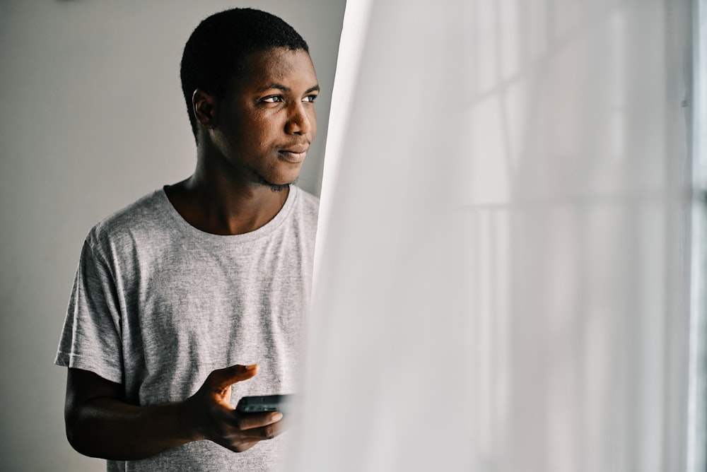 man in gray crew neck shirt standing beside white curtain