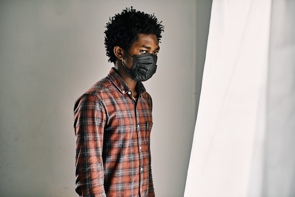 homme en chemise à carreaux rouge, noir et blanc, portant un masque noir