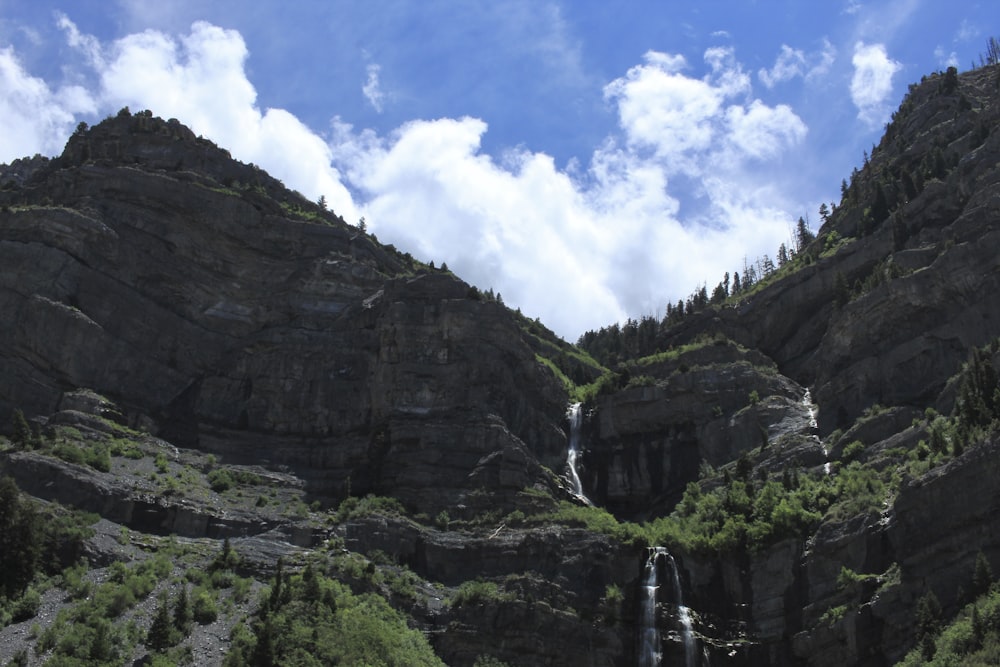 waterfalls between rocky mountain under blue and white cloudy sky during daytime