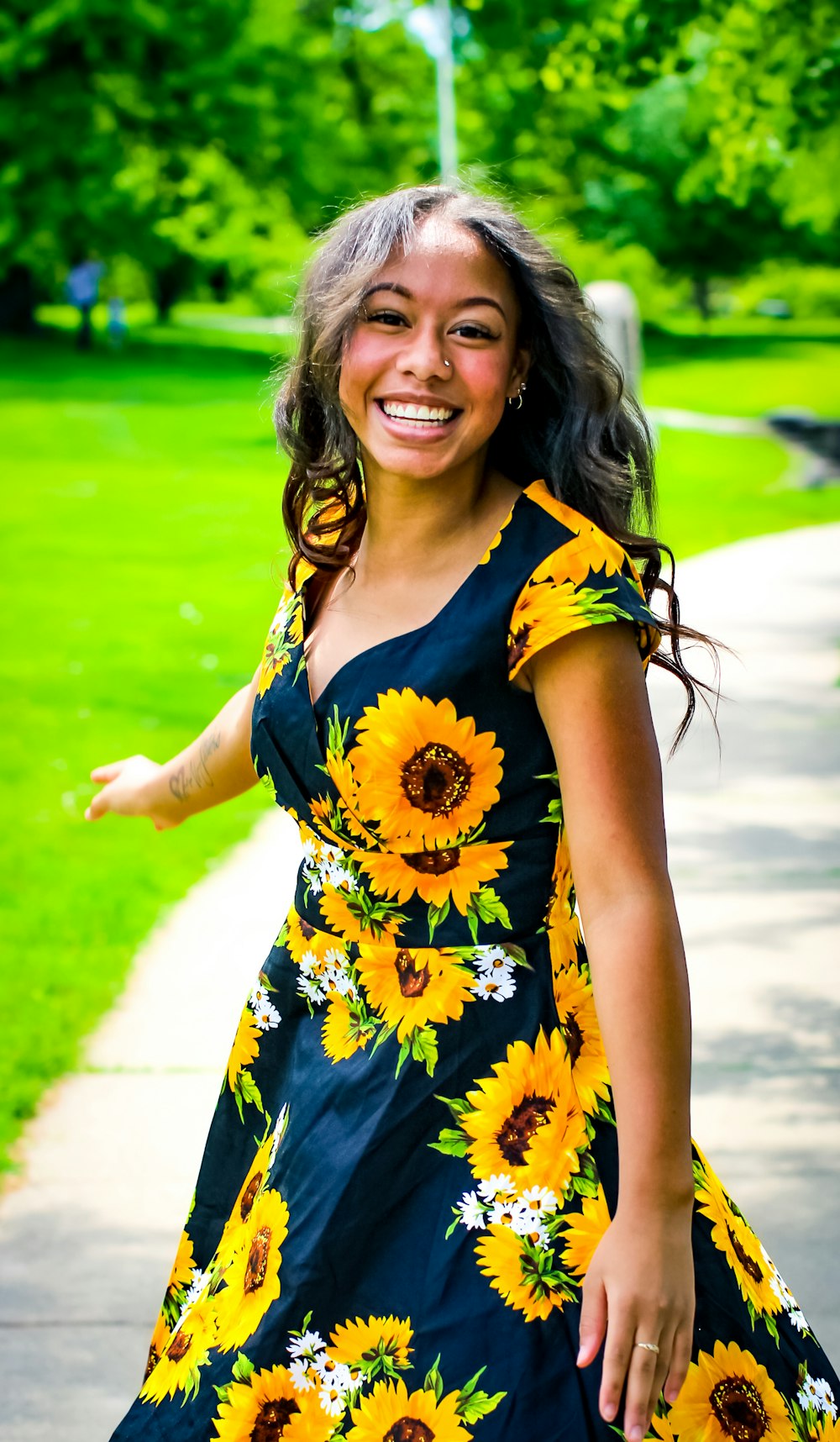 smiling woman in blue and yellow floral dress standing on pathway during daytime