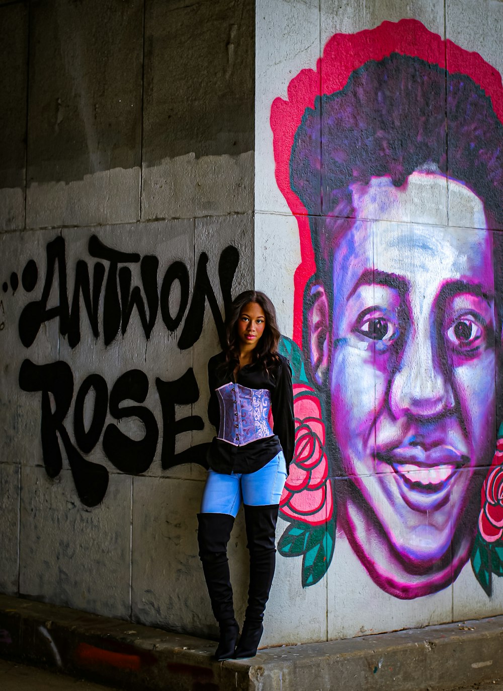 mulher na jaqueta preta e rosa encostada na parede com grafite