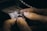 Hands holding and working on a piece of jewelry, possibly a ring, with intricate details and small spikes, against a blurred background of a workbench.