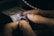 Hands holding and working on a piece of jewelry, possibly a ring, with intricate details and small spikes, against a blurred background of a workbench.