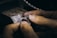 Hands holding and working on a piece of jewelry, possibly a ring, with intricate details and small spikes, against a blurred background of a workbench.