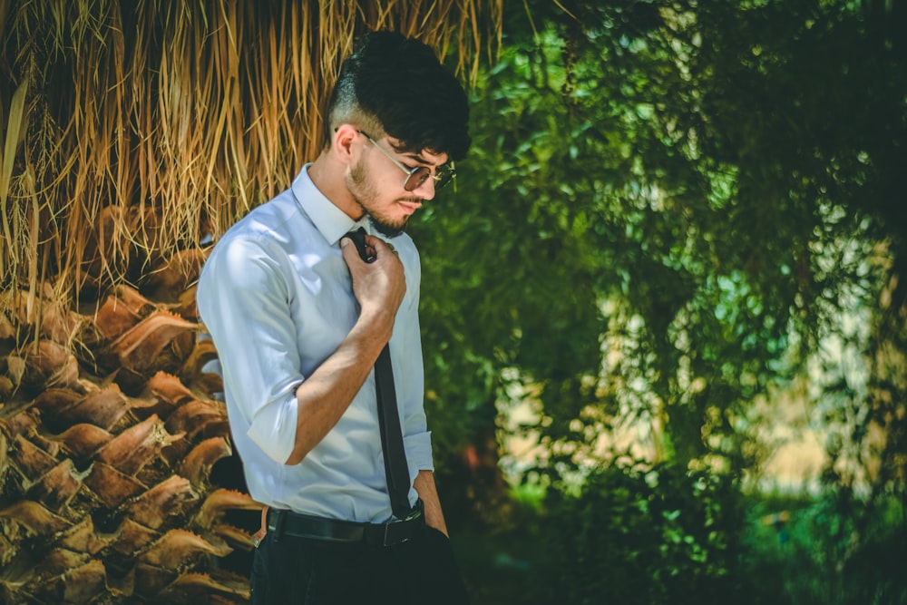 man in white dress shirt and black pants standing near green trees during daytime