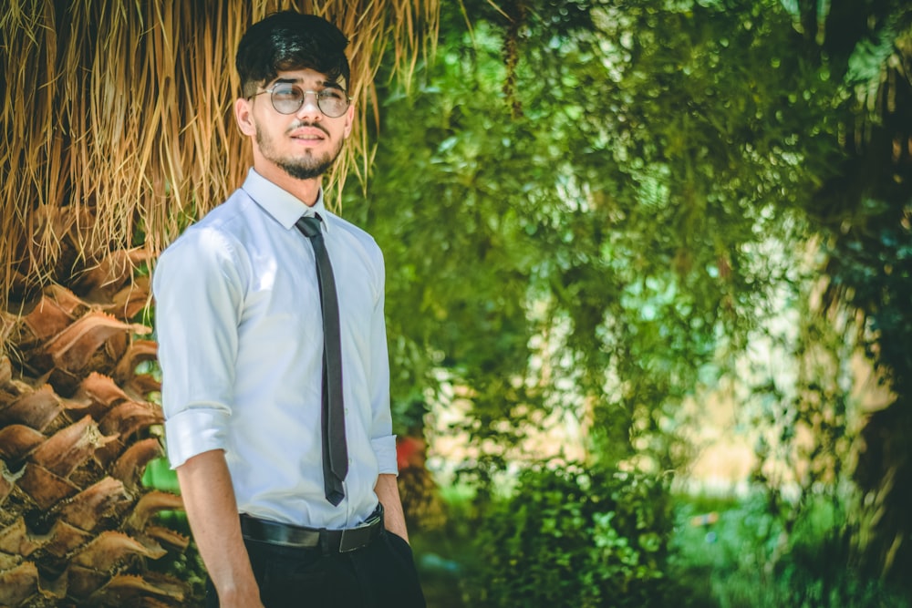 man in white dress shirt and black pants standing near green trees during daytime