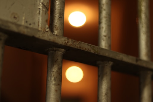 Metal bars in close-up with defocused warm lights in the background, suggesting a dimly lit environment.