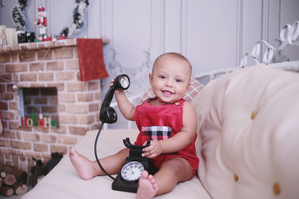 baby in red shirt sitting on white textile