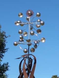 Completed metal sculpture displayed outdoors, reflecting sunlight.