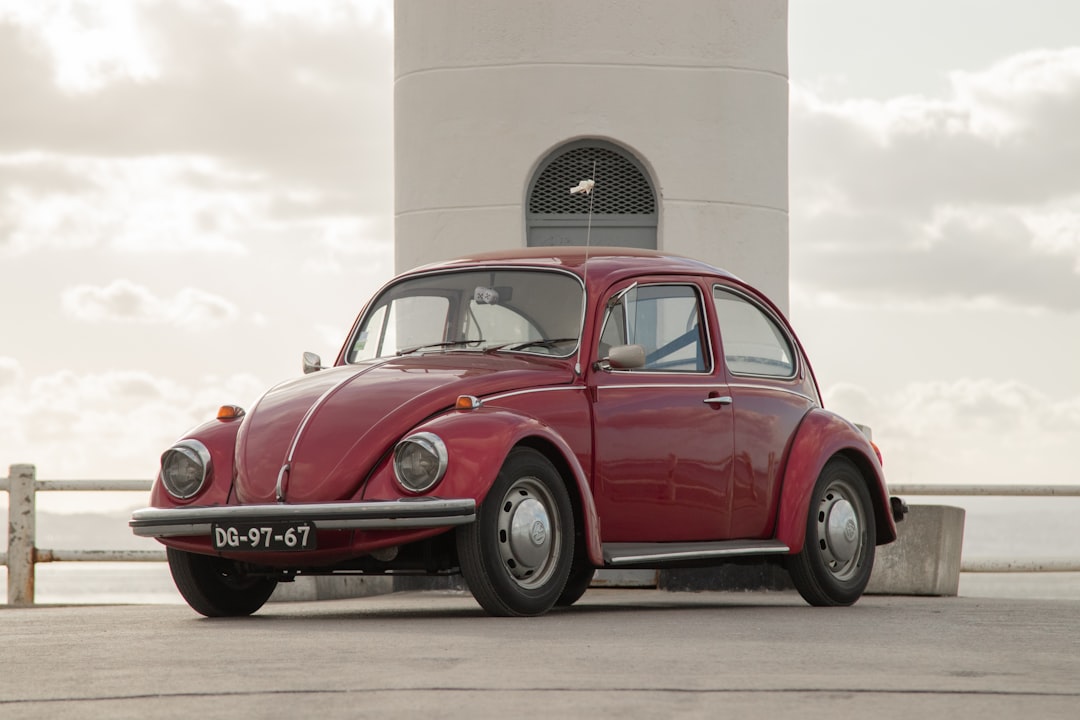 red volkswagen beetle parked beside white concrete building during daytime