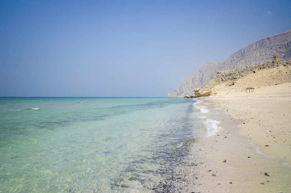 blue sea beside brown mountain under blue sky during daytime