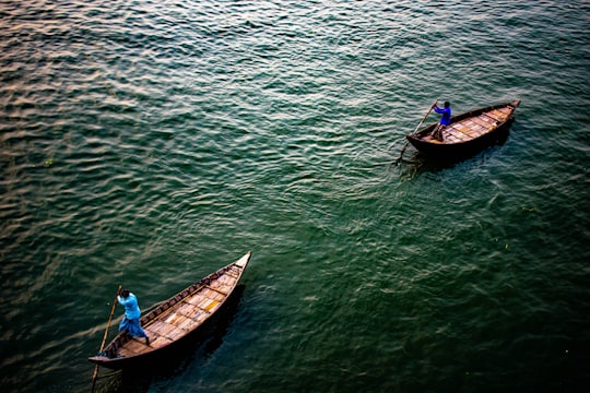 man in blue shirt riding on brown wooden boat on green water during daytime in Dhaka Bangladesh