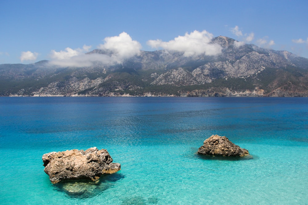 brown and black rock formation on blue sea water under white clouds and blue sky during