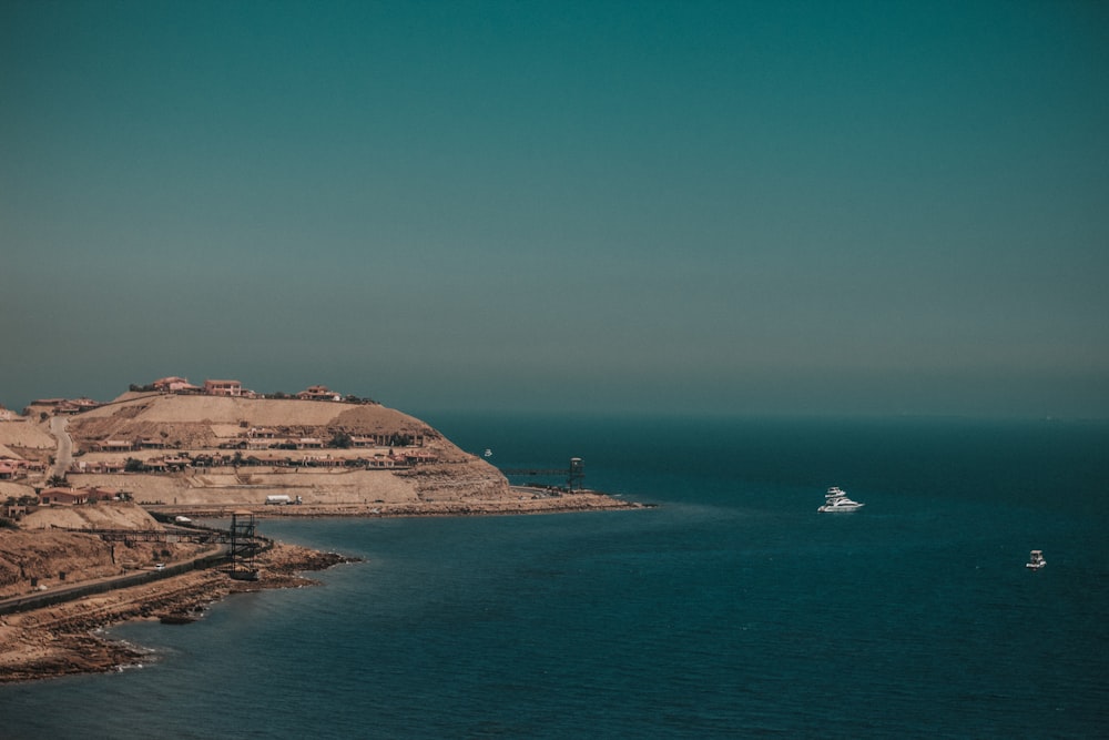 white boat on sea near brown mountain under blue sky during daytime