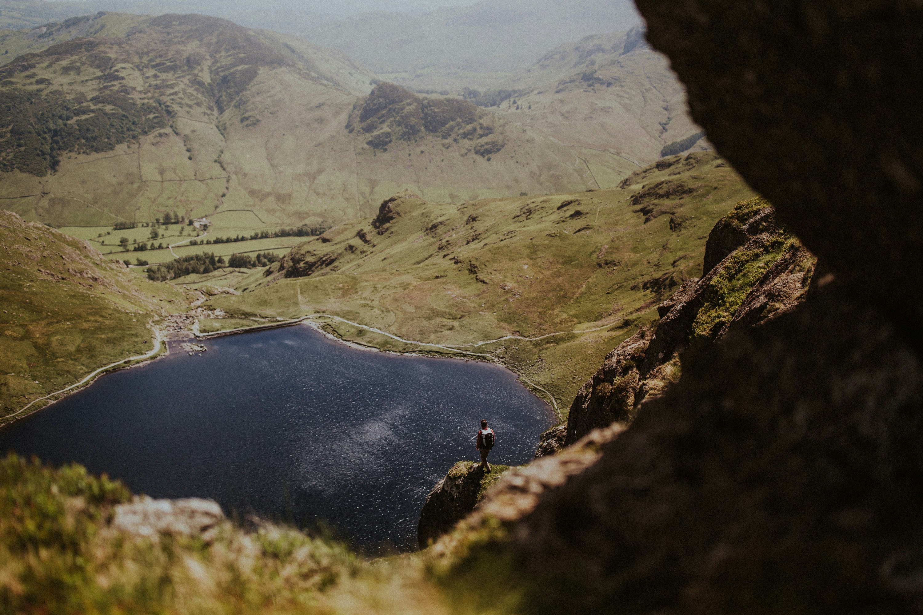 person in black jacket standing on rock formation near lake during daytime