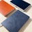 Three hardcover notebooks with textured covers are arranged on a light surface. The notebooks are in different colors: orange, blue, and grey.
