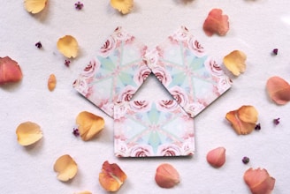 A delicate arrangement of blush pink greeting cards and bookmarks with floral accents, resting on a softly textured cream paper background.