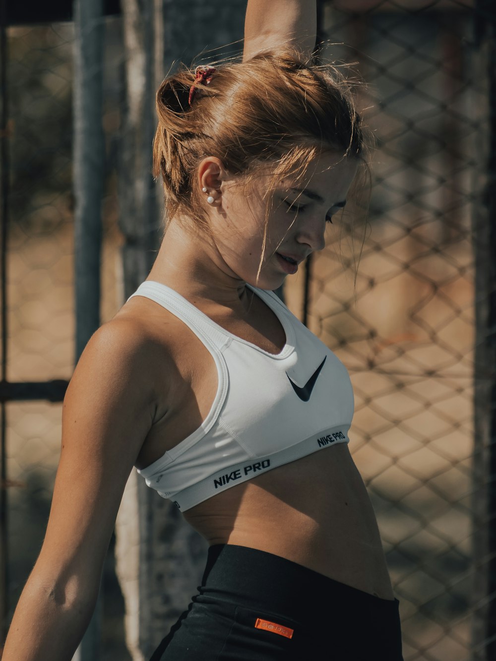 woman in white sports bra and black panty leaning on chain link fence during daytime