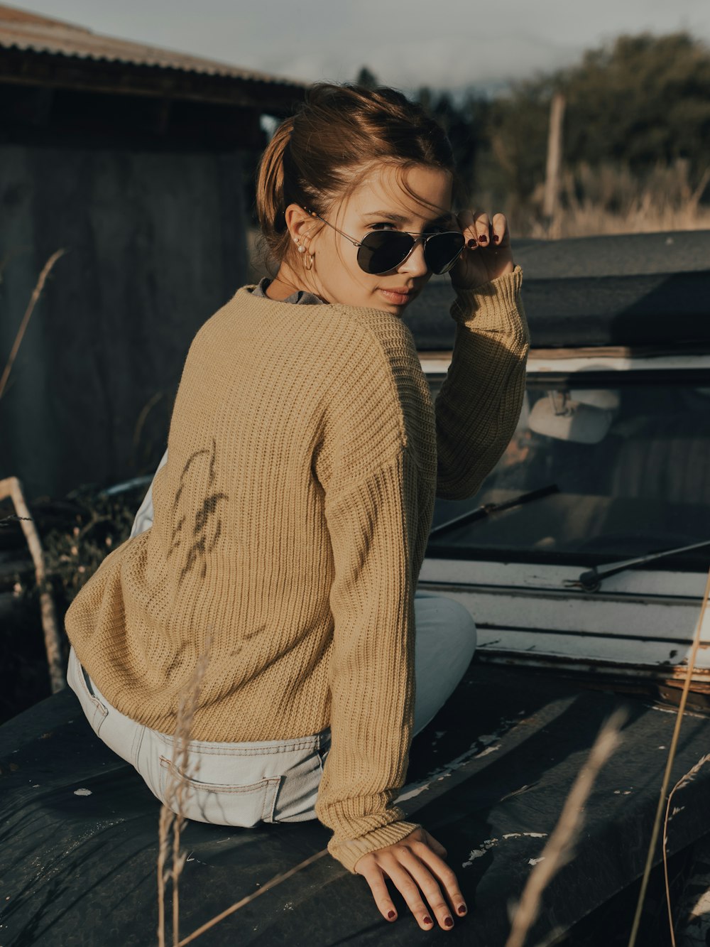 woman in brown sweater and white pants wearing black sunglasses
