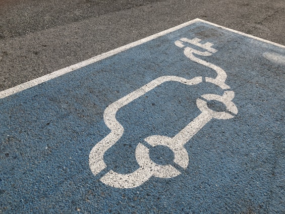 A blue parking space is marked with a white line drawing of an electric car and a charging plug, indicating a designated spot for electric vehicle charging.